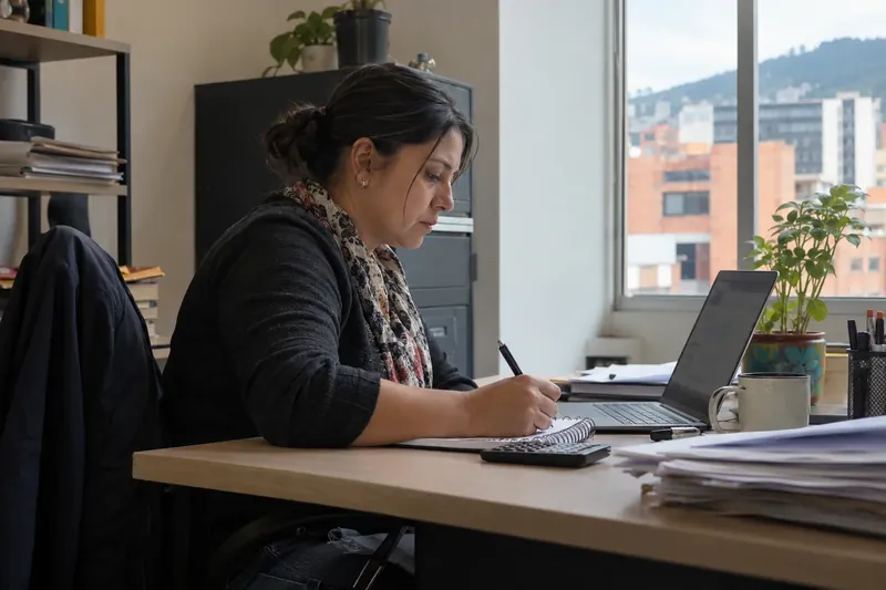 Precios de automatización con IA: dueña de una pyme revisa los planes en el portátil y anota en su libreta