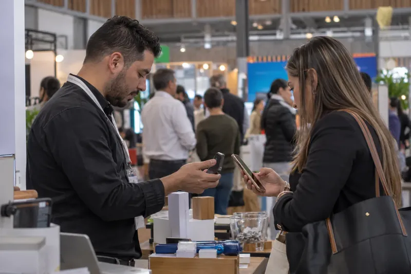 Tarjeta de presentación digital: dos personas comparten el contacto con el celular en una feria